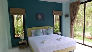A bedroom with a large bed, two windows with curtains, a small bedside table, and a view of greenery outside. - Phuket Sirinapha Resort (Sa Khu)