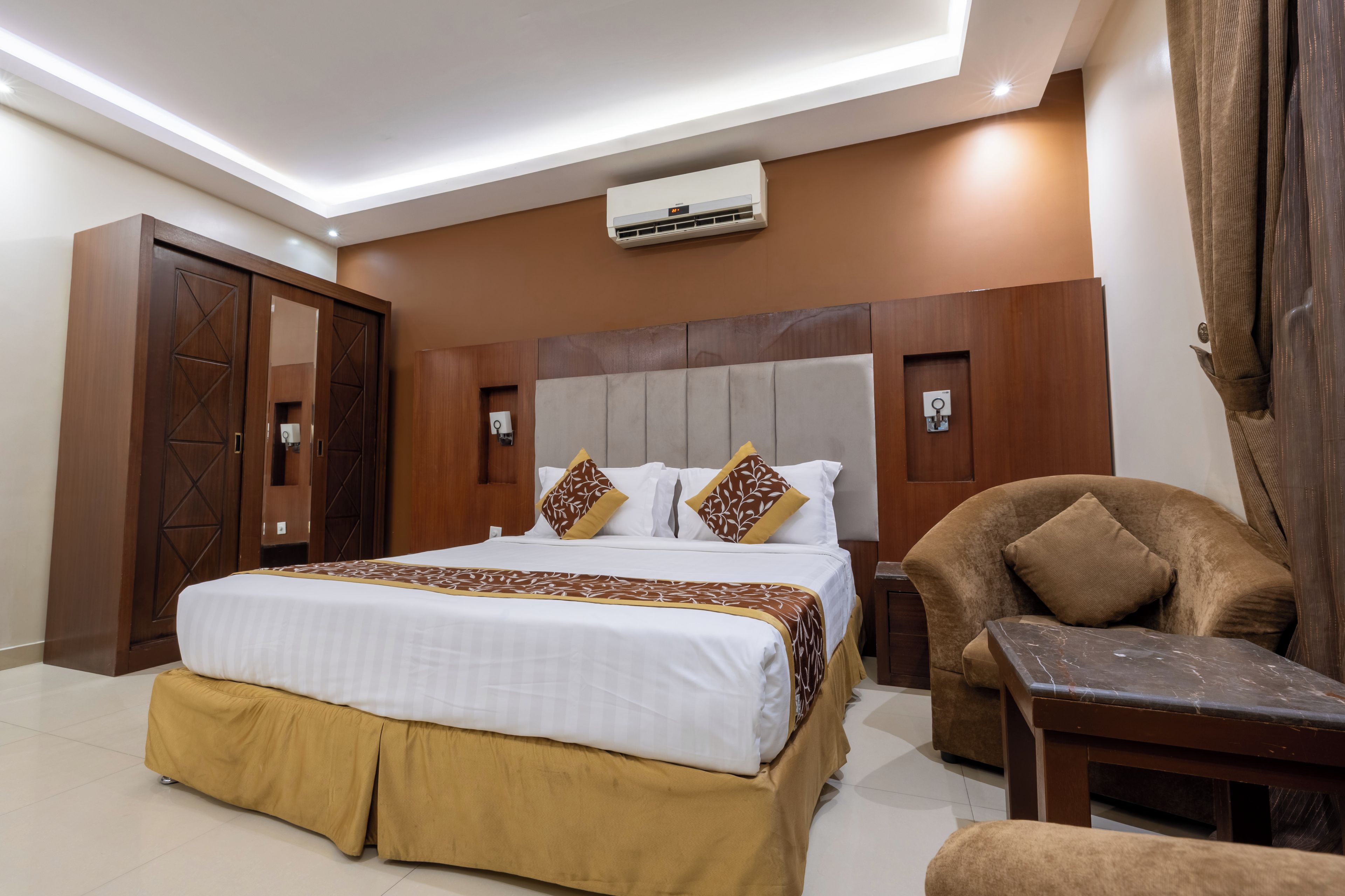 Una habitación de hotel con cama, una silla, una mesita de noche y un equipo de aire acondicionado.