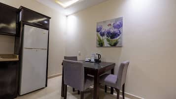 Una cocina compacta con refrigerador, una mesa de comedor con cuatro sillas y un cuadro en la pared.