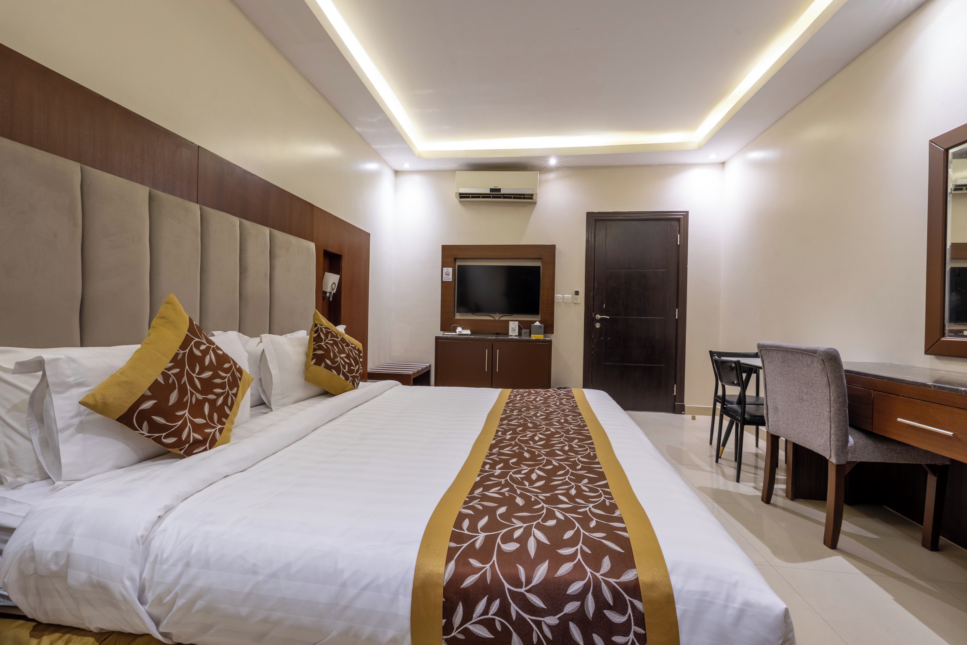 A hotel room with a large bed, a desk, a chair, a television, and a wardrobe.