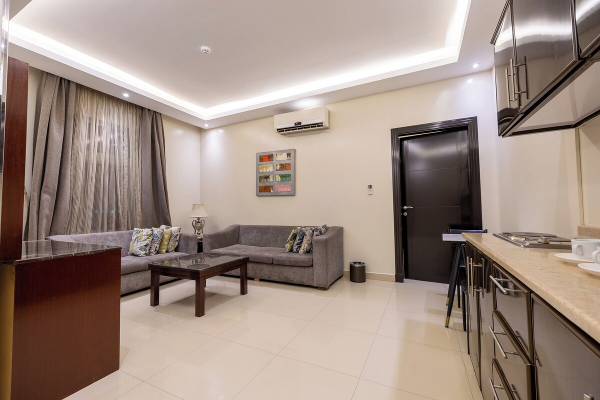 A modern living room with a sofa, coffee table, and a dining area with a kitchen counter.