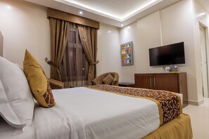 Quarto de hotel com cama, televisão, escrivaninha e uma cadeira.