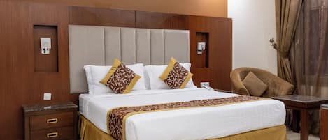 A hotel room with a large bed, bedside tables, a desk, and an air conditioning unit on the wall.