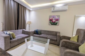 A modern living room with a sofa, armchair, glass coffee table, and an air conditioning unit.