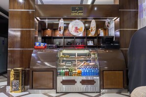 A coffee shop counter with a variety of snacks and beverages, a coffee machine, and a sign indicating the shop's name. - Al Muhaidb Residence Al Malaz 1 - Economic (Riyadh)