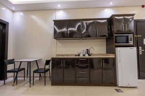 A compact kitchen with dark wooden cabinets, a microwave, a refrigerator, and a small dining area with two chairs and a table. - Al Muhaidb Residence Al Malaz 1 - Economic (Riyadh)