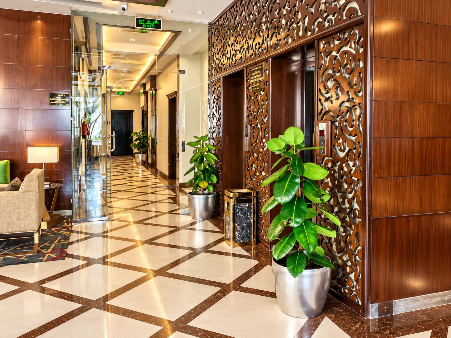 A hotel lobby with a checkered floor, potted plants, a reception desk, and a decorative wall.