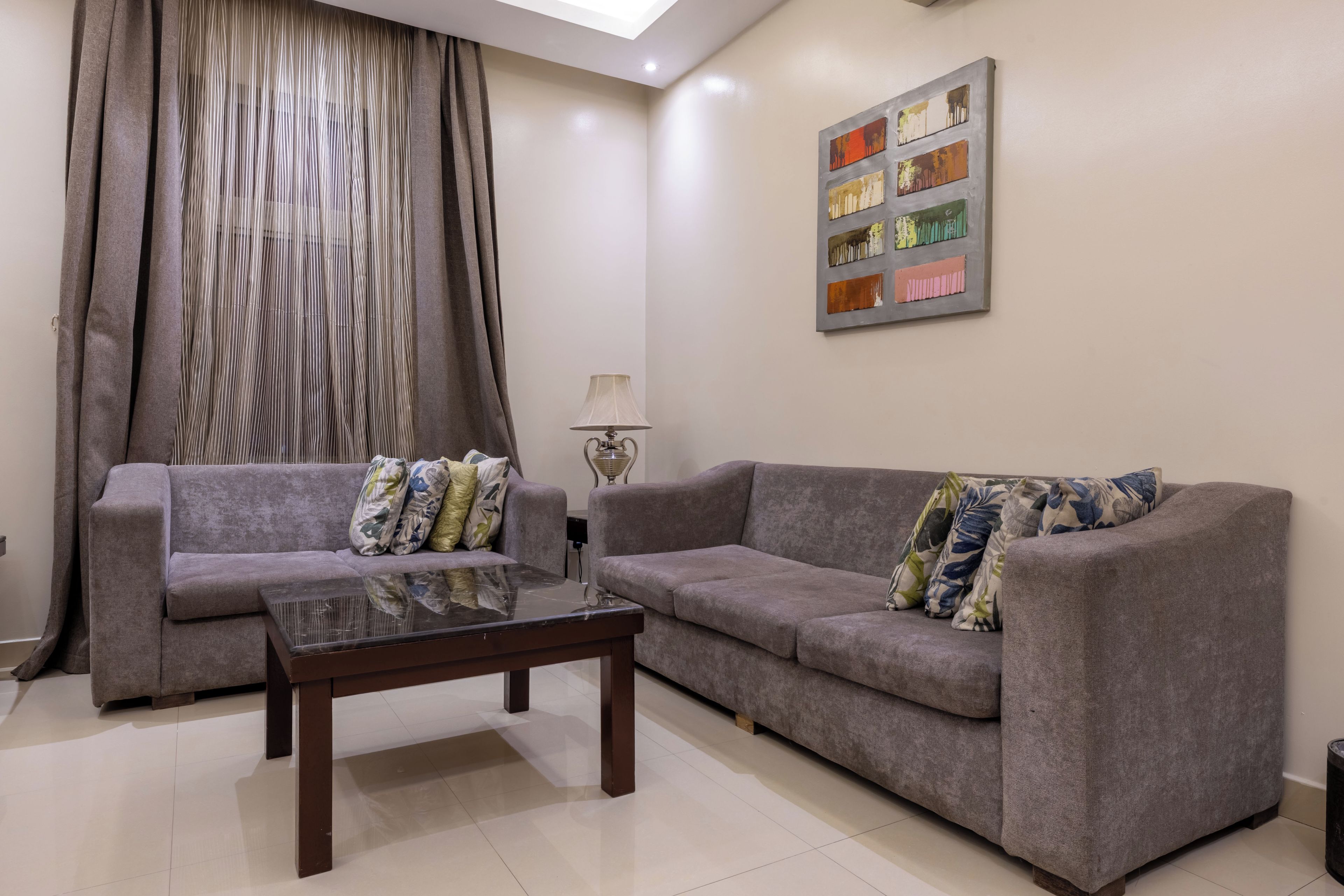 A living room with two grey sofas, a glass coffee table, and a lamp.
