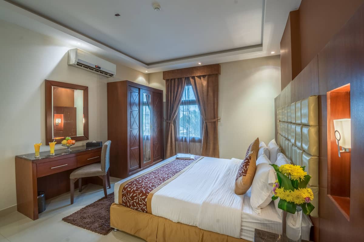 A hotel room with a bed, a desk, a chair, a wardrobe, and a large mirror.