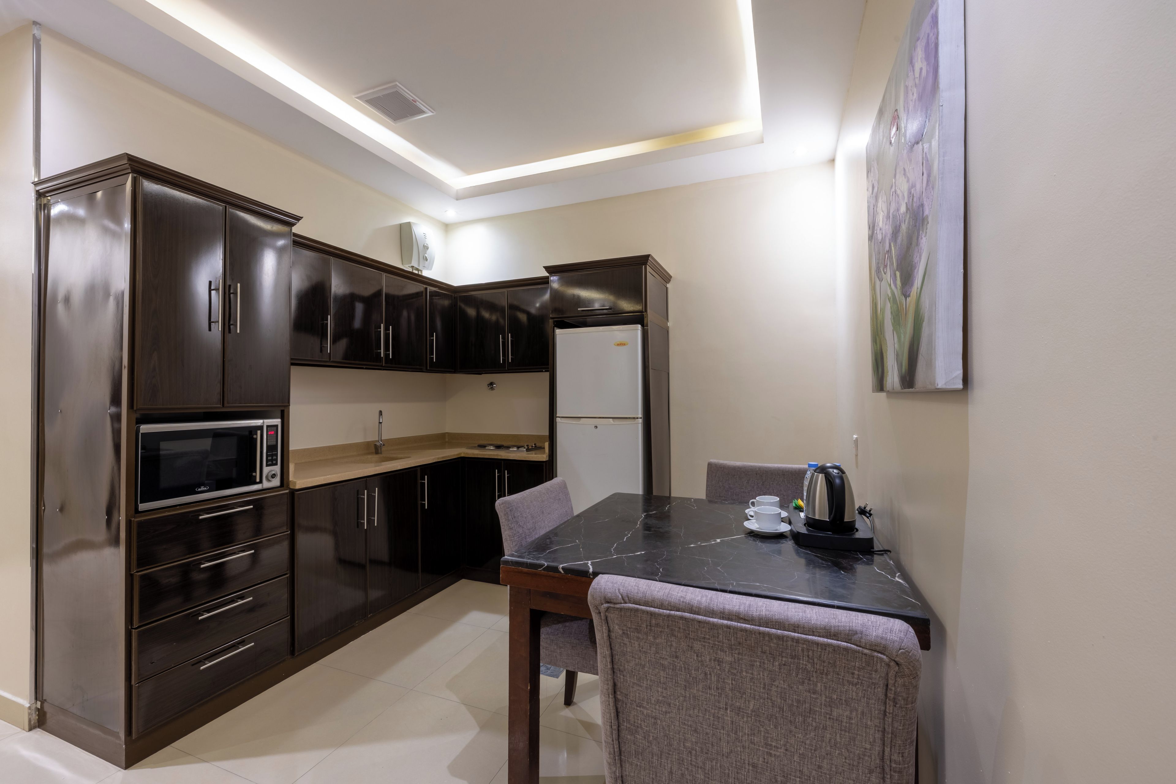 Una cocina compacta con armarios oscuros, microondas, pileta y comedor con mesa y sillas.