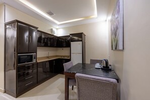 Una cocina compacta con armarios oscuros, microondas, pileta y comedor con mesa y sillas.