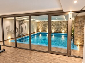 A modern indoor swimming pool with a stone wall and exercise equipment. - Al Muhaidb Residence Al Malaz 1 - Economic (Riyadh)