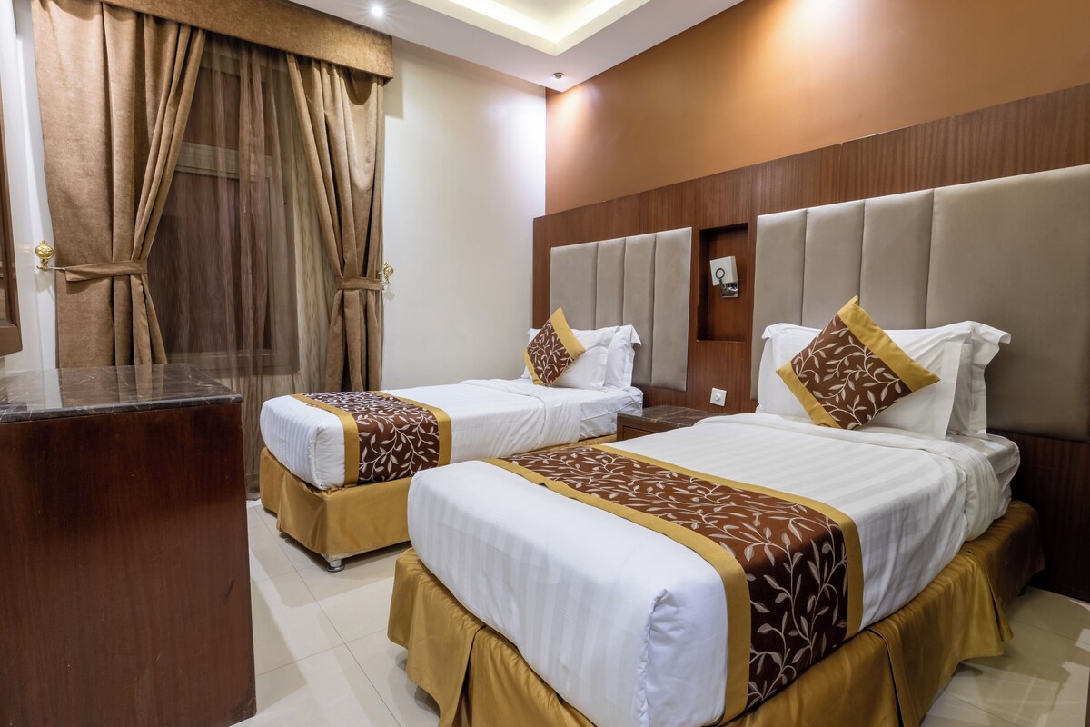 A hotel room with two beds, a wooden headboard, a mirror, and a window with curtains.