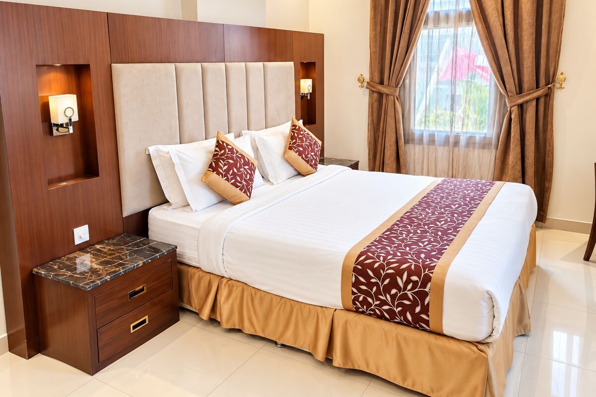 A hotel room with a bed, nightstands, a marble-topped dresser, and a window with curtains.