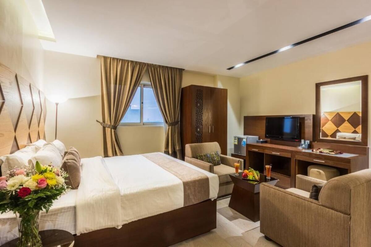 A hotel room with a bed, a desk with a TV, a chair, and a window with curtains.
