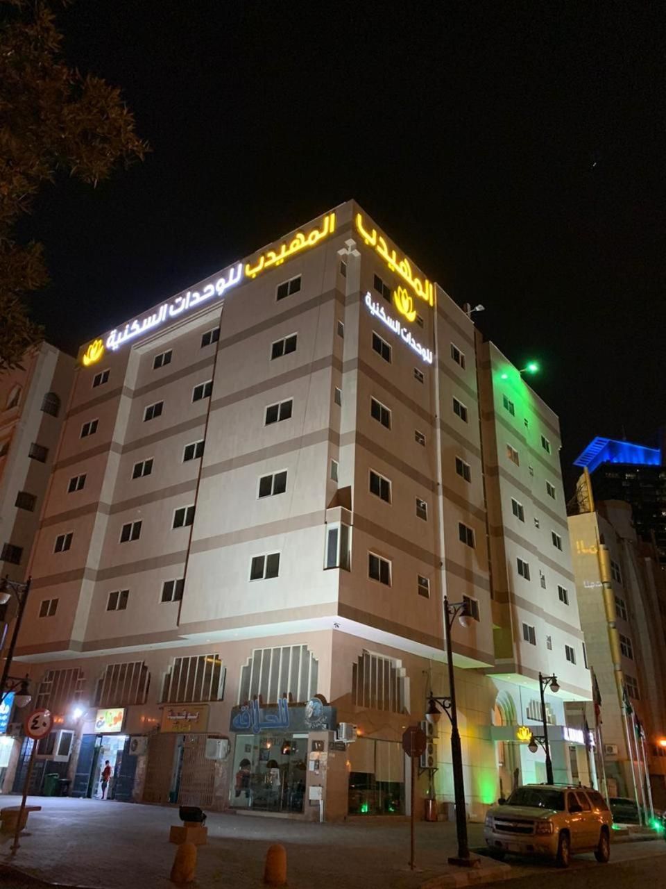 Un hotel de varios pisos con señalización iluminada, una entrada a nivel de calle y un estacionamiento visible.