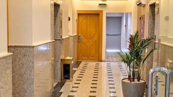 A hotel corridor with a polished tile floor, a potted plant, and an exit sign.