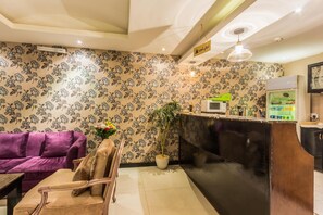 A reception area with a purple sofa, a wooden chair, a potted plant, a black counter, and a sign above the counter. - Al Muhaidb Residence Al olaya 2 - Economic (Riyadh)