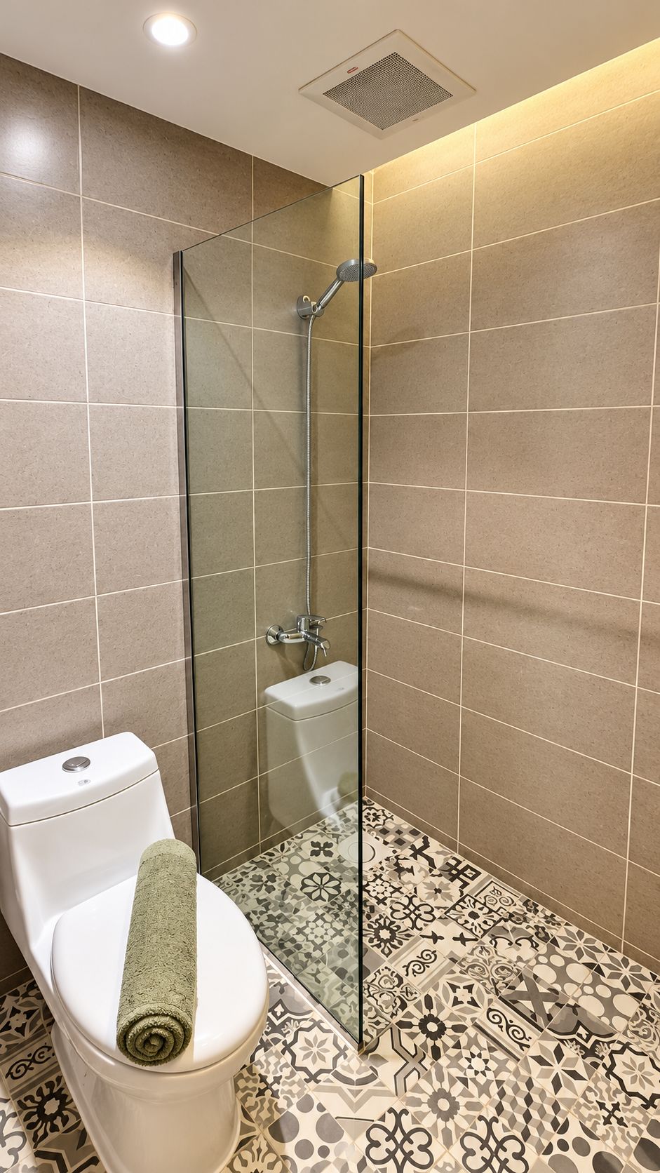 A bathroom with a glass-enclosed shower, a toilet with a towel, and patterned floor tiles.