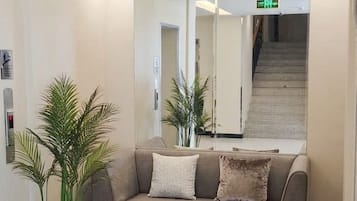 A modern lobby with a sofa, potted plants, a mirror, and a staircase.