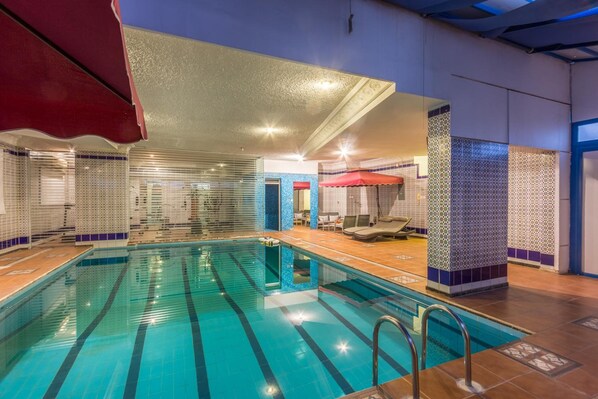 Una piscina interior con carriles delimitados, una sombrilla roja y paredes de azulejos.