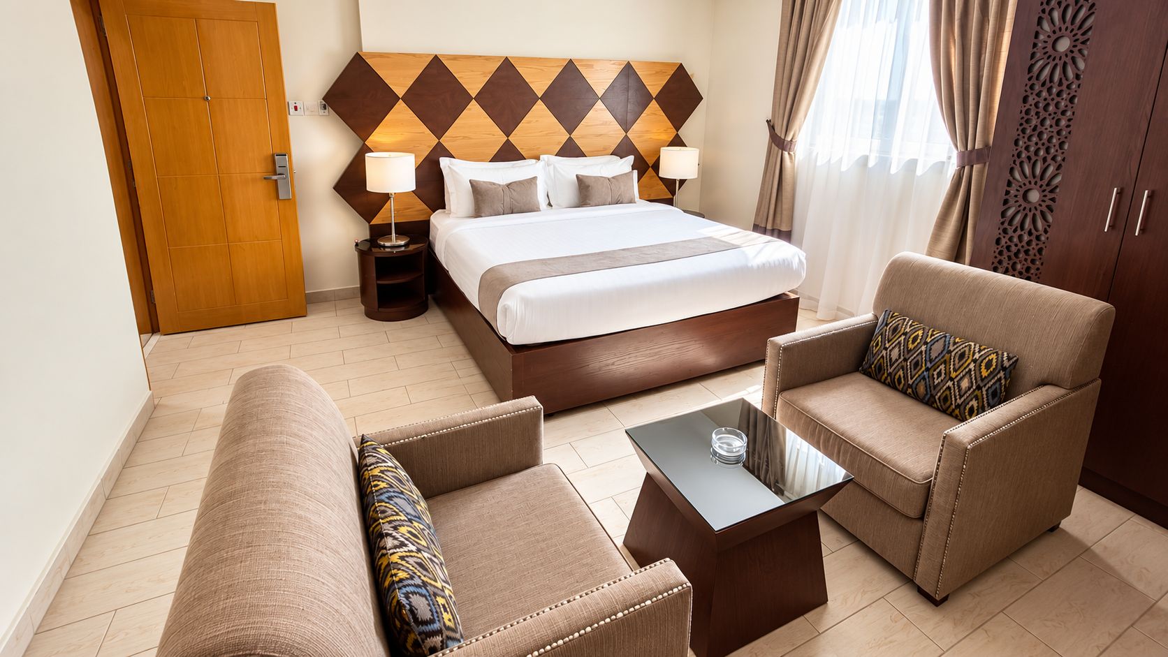 A hotel room with a bed, two armchairs, a coffee table, and a wooden wardrobe.