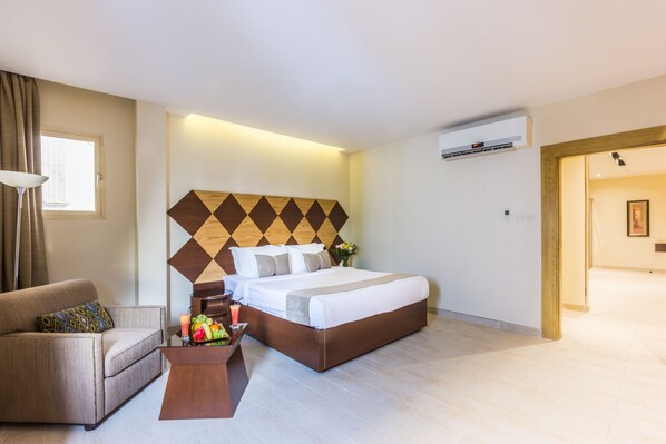A hotel room with a large bed, a sofa, a small table with fruit and a drink, and a window with curtains. - Al Muhaidb Residence Al olaya 2 - Economic (Riyadh)