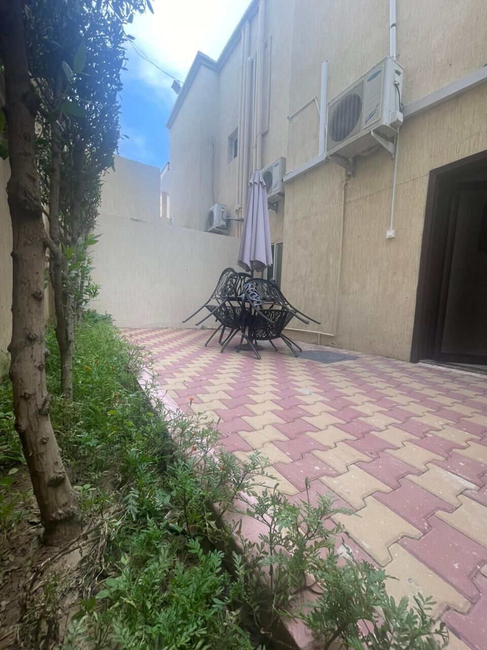 A building with air conditioning units, a tiled patio, and a metal table with chairs.