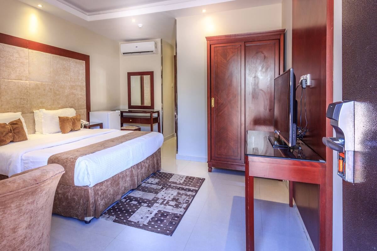 A hotel room with a large bed, a desk, a television, and a wardrobe.