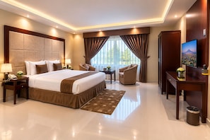 A hotel room with a large bed, bedside tables, a desk, a chair, a TV, and a view of the outdoors.