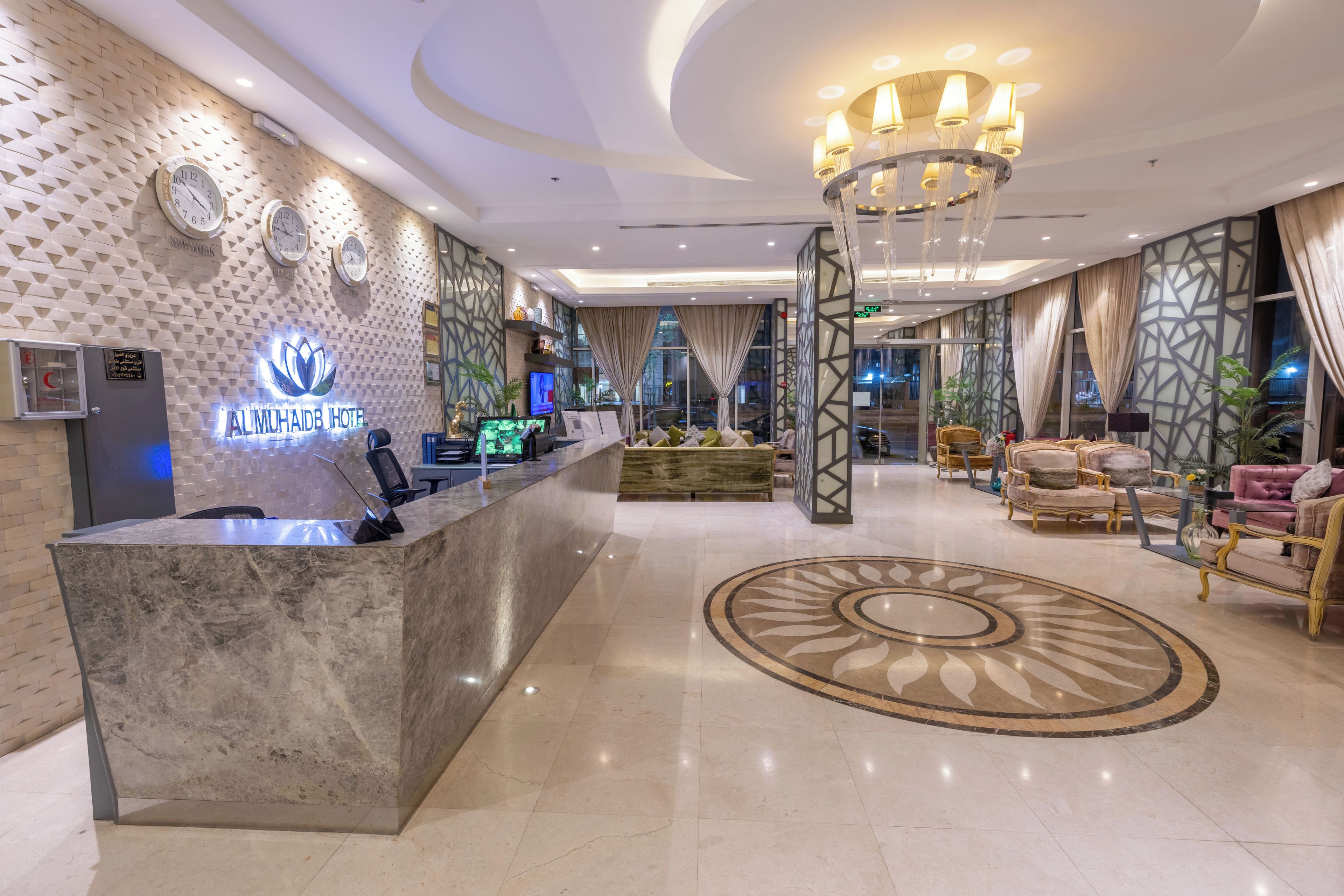 A hotel lobby with a reception desk, a chandelier, and a seating area with sofas and chairs.