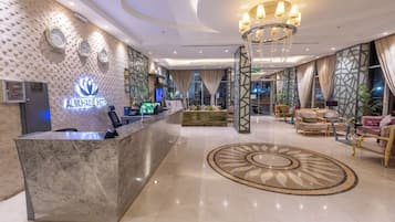 A hotel lobby with a reception desk, a chandelier, and a seating area with sofas and chairs.