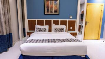 A hotel room with a large bed, a wooden headboard, a painting on the wall, and a door to the right.