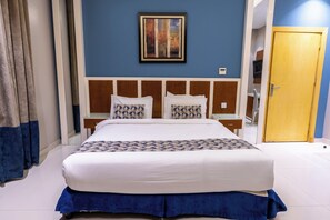 A hotel room with a large bed, a wooden headboard, a painting on the wall, and a door to the right.