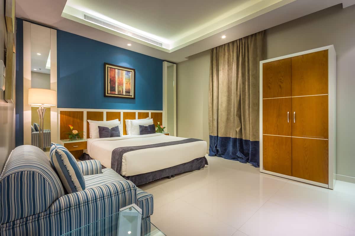Una habitación de hotel moderna con una cama grande, un sofá, un armario y una mesita de noche con una lámpara.