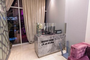 Un mostrador de recepción con encimera de mármol, separador de vidrio y un cartel que indica un centro de negocios.