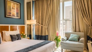 A hotel room with a large bed, a striped armchair, a vase with flowers, and a painting on the wall. - Al Muhaidb Residence Al Malaz 2 - Economic (Riyadh)