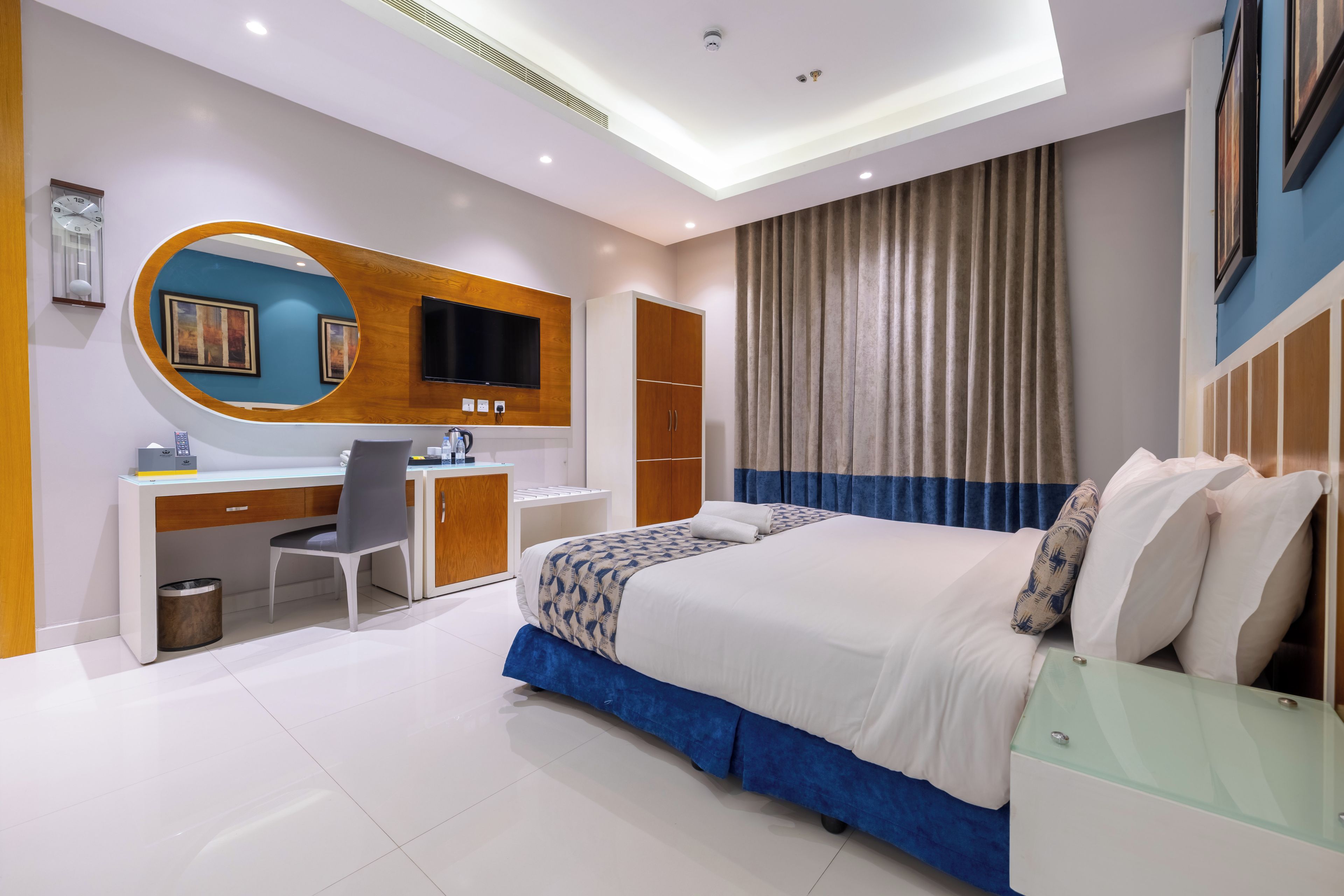 A modern hotel room with a large bed, a desk with a chair, a television, and a wardrobe.