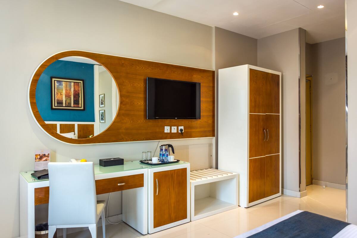Una habitación de hotel moderna con un escritorio de madera, un televisor de pantalla plana y un armario.