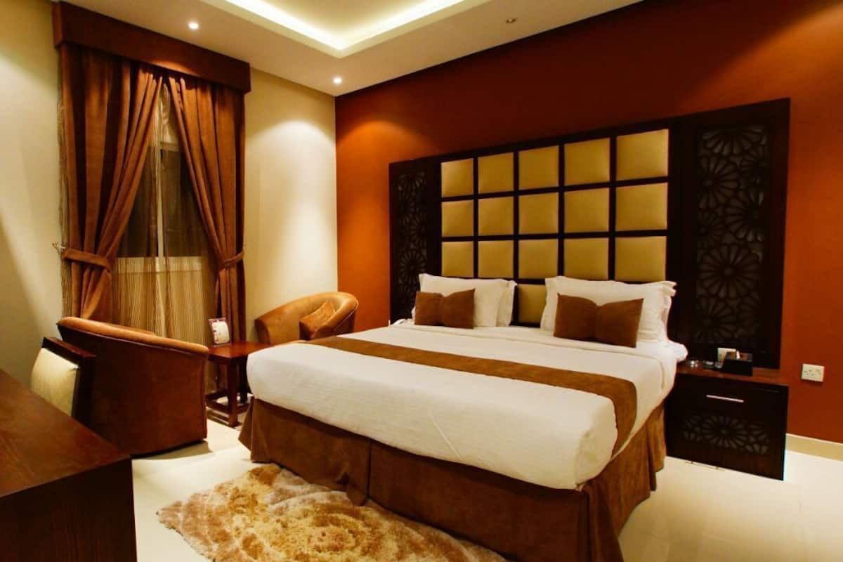 A bedroom with a large bed, a nightstand, a chair, and a wooden desk.