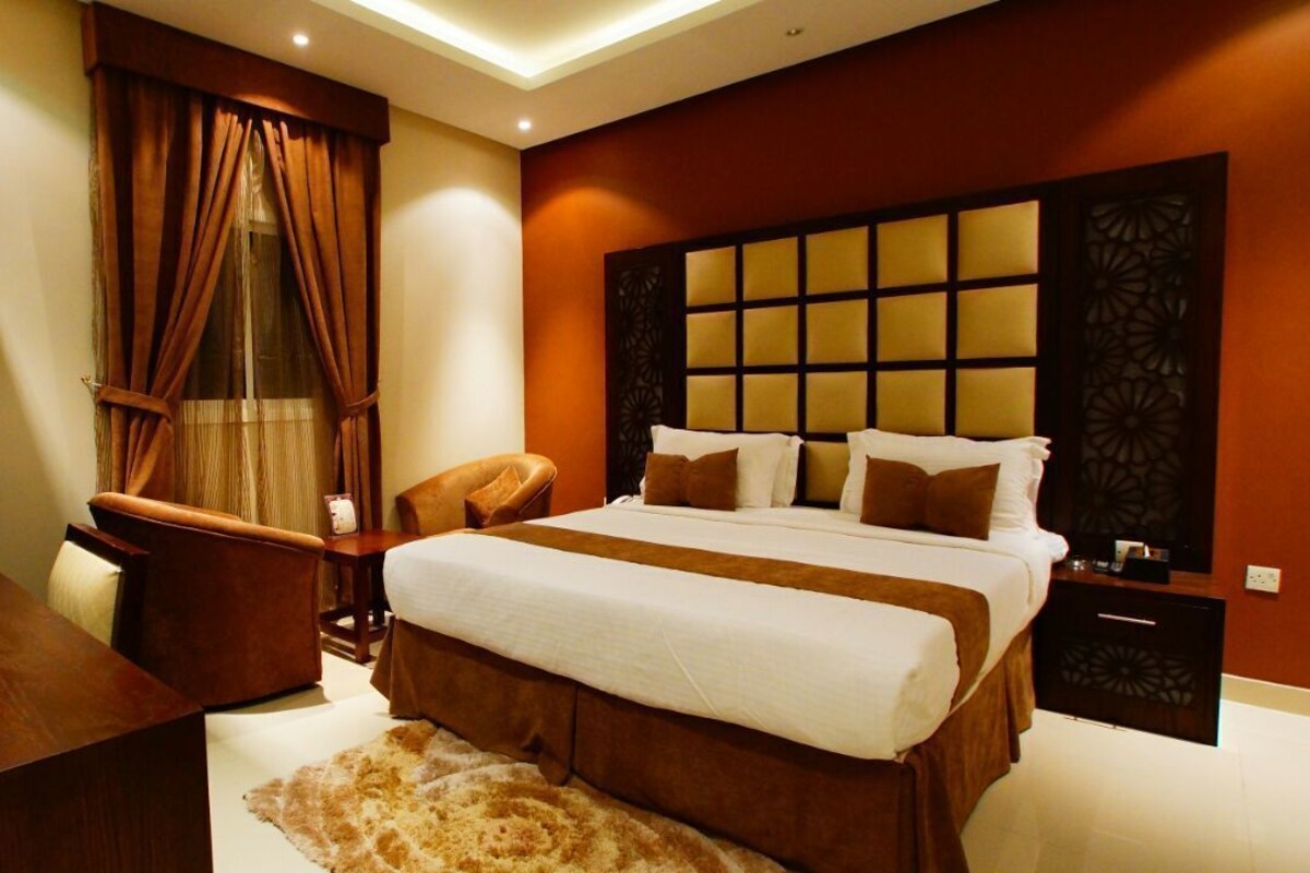A bedroom with a large bed, a nightstand, a chair, and a wooden desk.