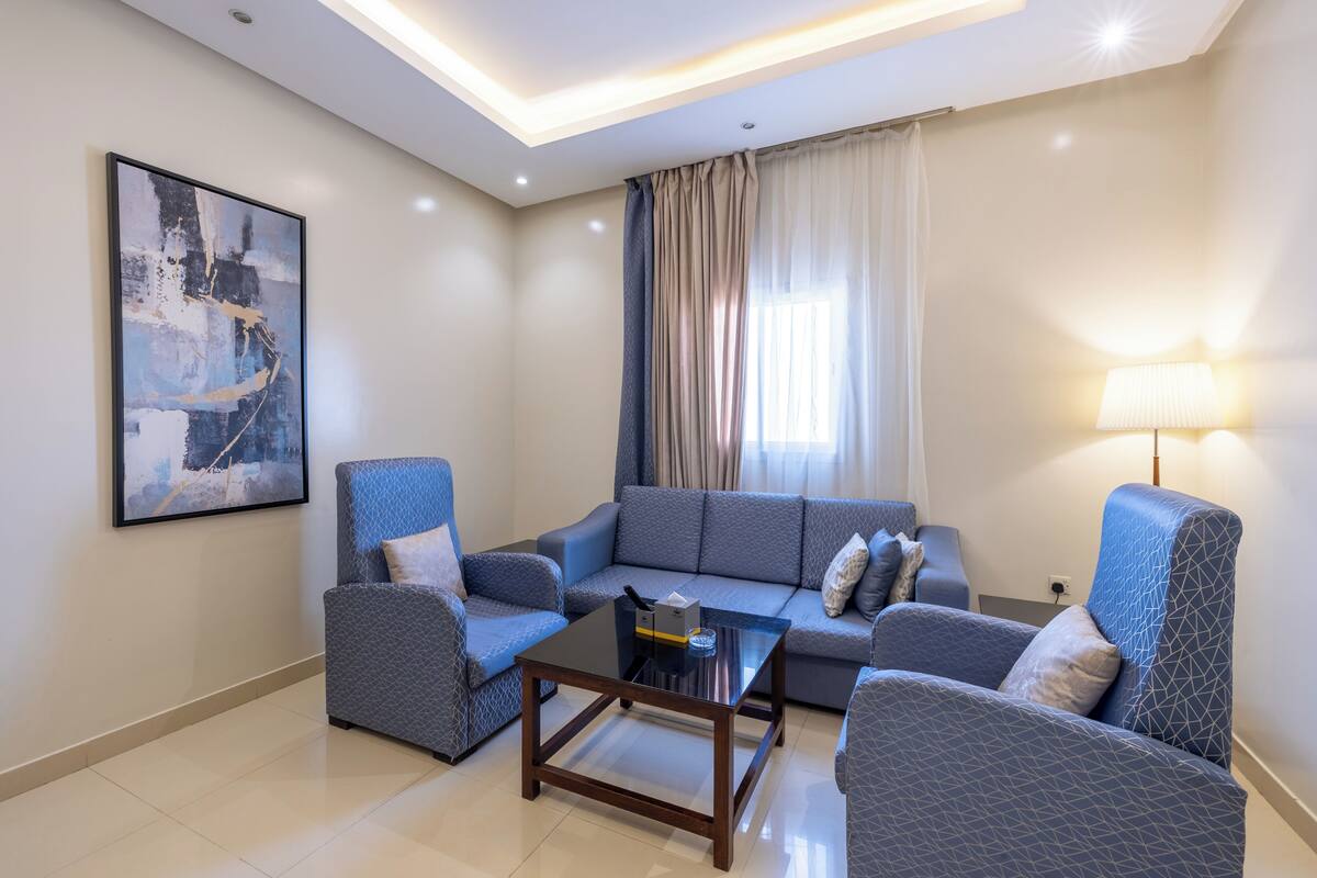 A living room with a sofa, two armchairs, a coffee table, a painting on the wall, and a lamp.