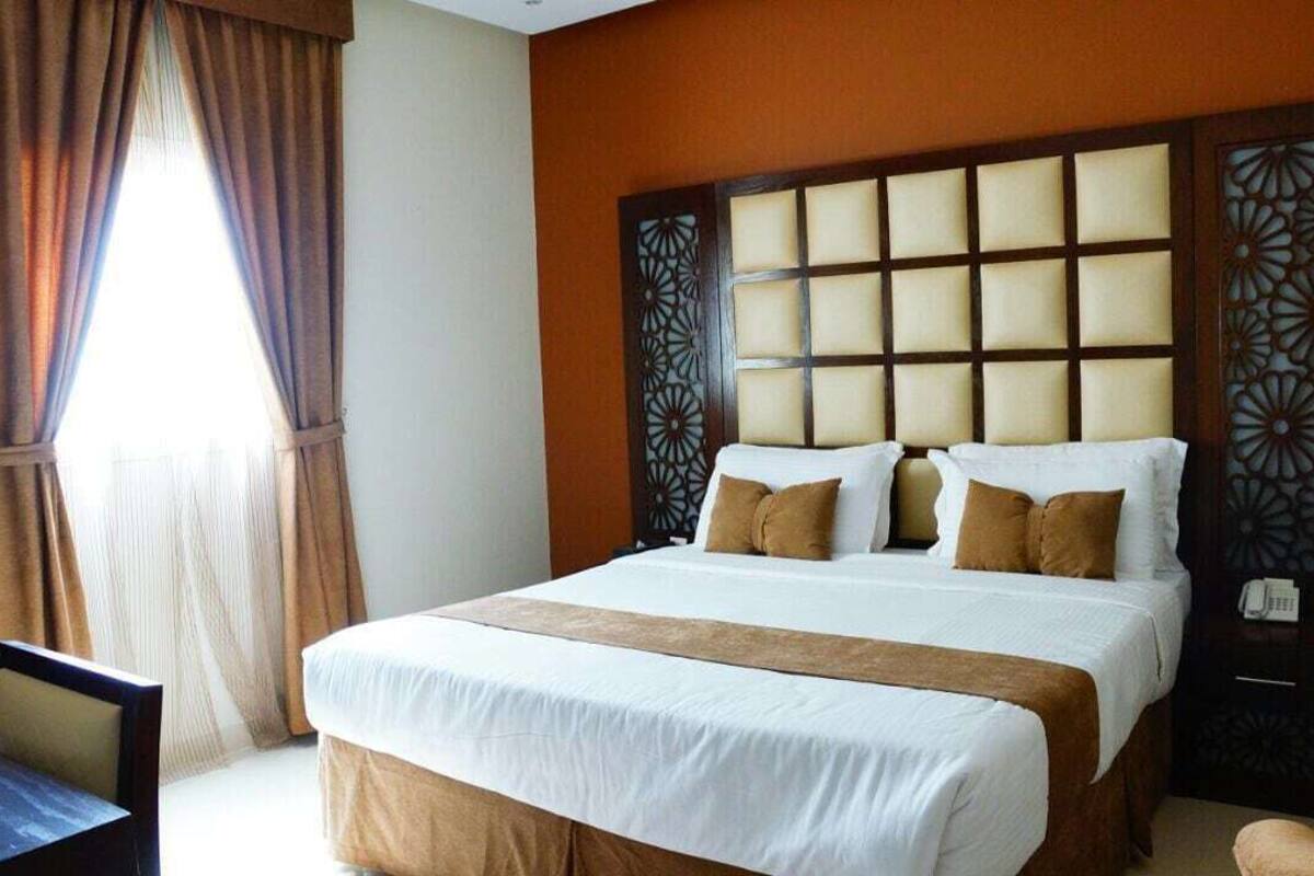 A hotel room with a large bed, a wooden headboard, a desk, and a chair.