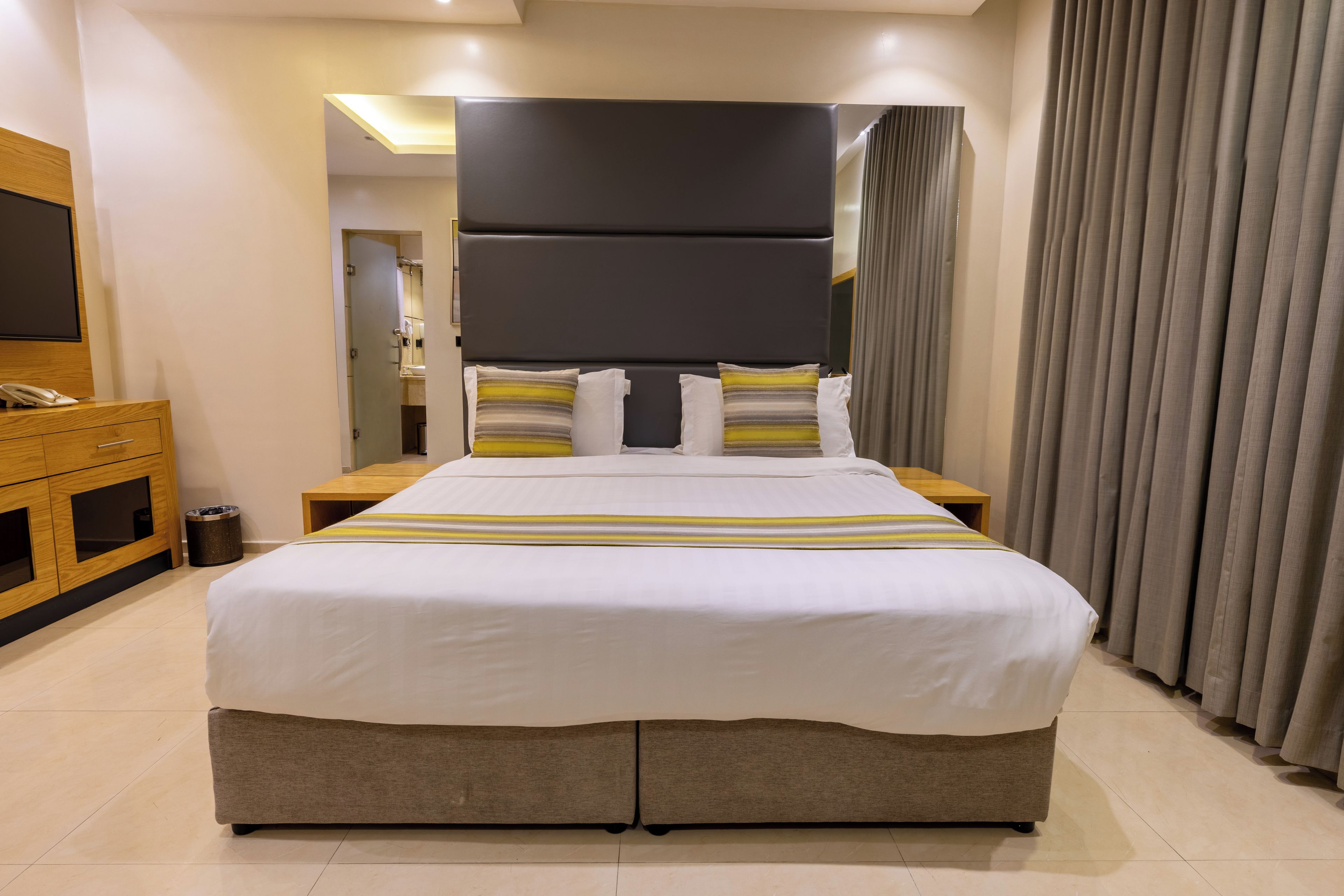 Hotellihuone, jossa on suuri sänky, puinen yöpöytä, sängyn vieressä oleva pöytä ja peili.