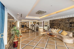 Un hall espacioso con piso de mármol, una recepción, una zona de estar con sofá y sillones, y una pared decorativa con candelabro.