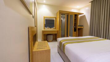 A hotel room with a bed, a wooden desk, a mirror, a wardrobe, and a small stool.