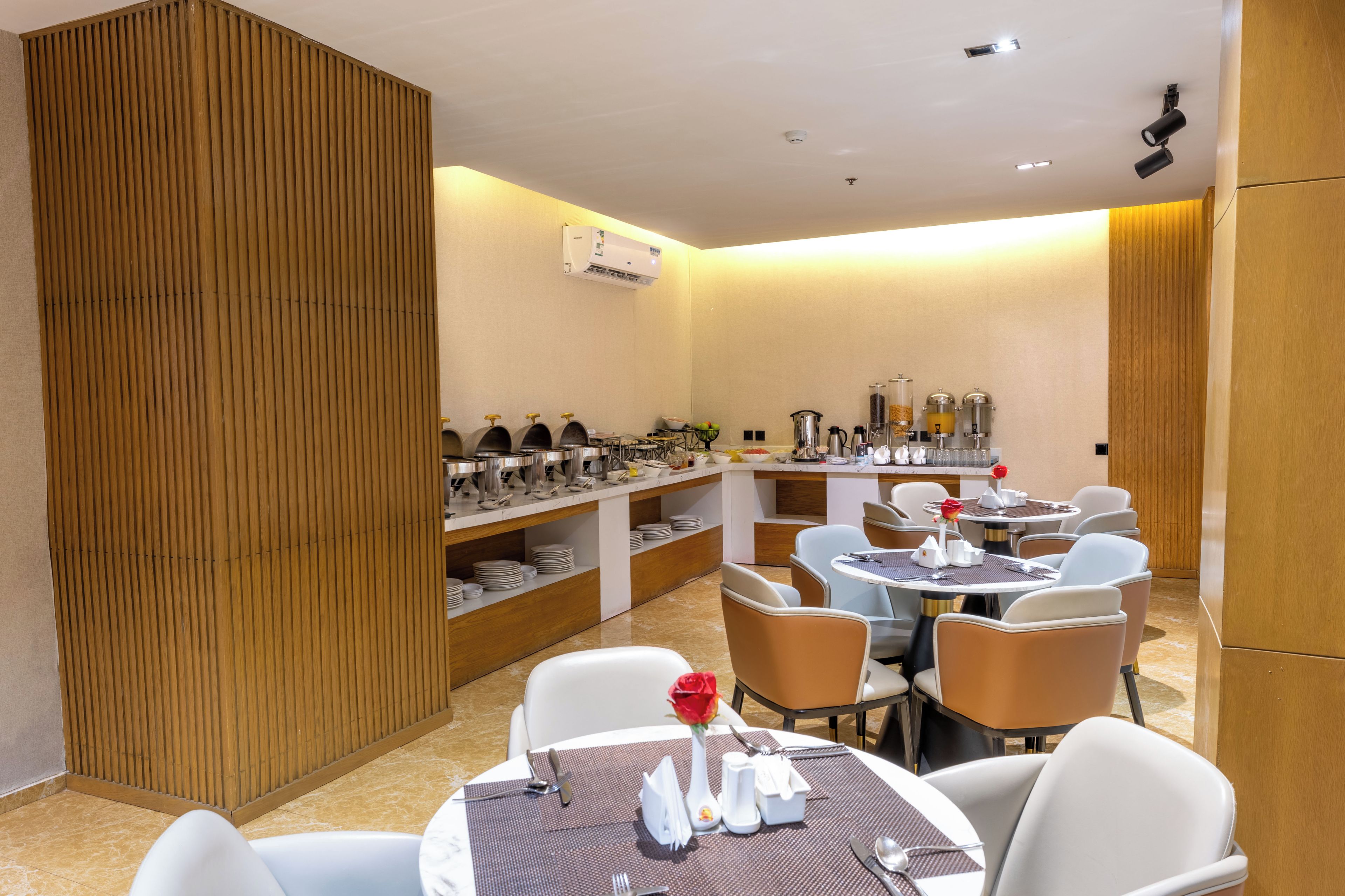 A restaurant with round tables, chairs, and a buffet area with food and drink dispensers.