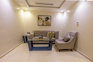 A living room with a sofa, armchair, and a glass coffee table. - Al MuhaidbResidence Al Takhasossi 1 - Economic (Riyadh)