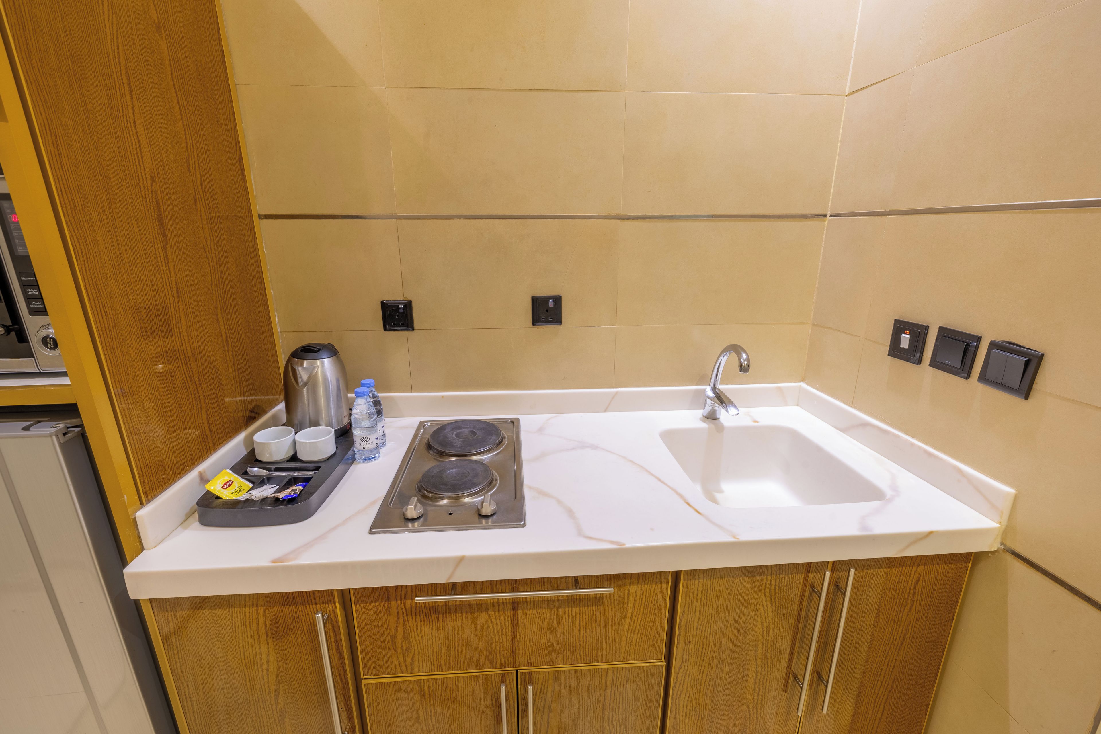 A kitchen with a white countertop, two sinks, a stove, and wooden cabinets.