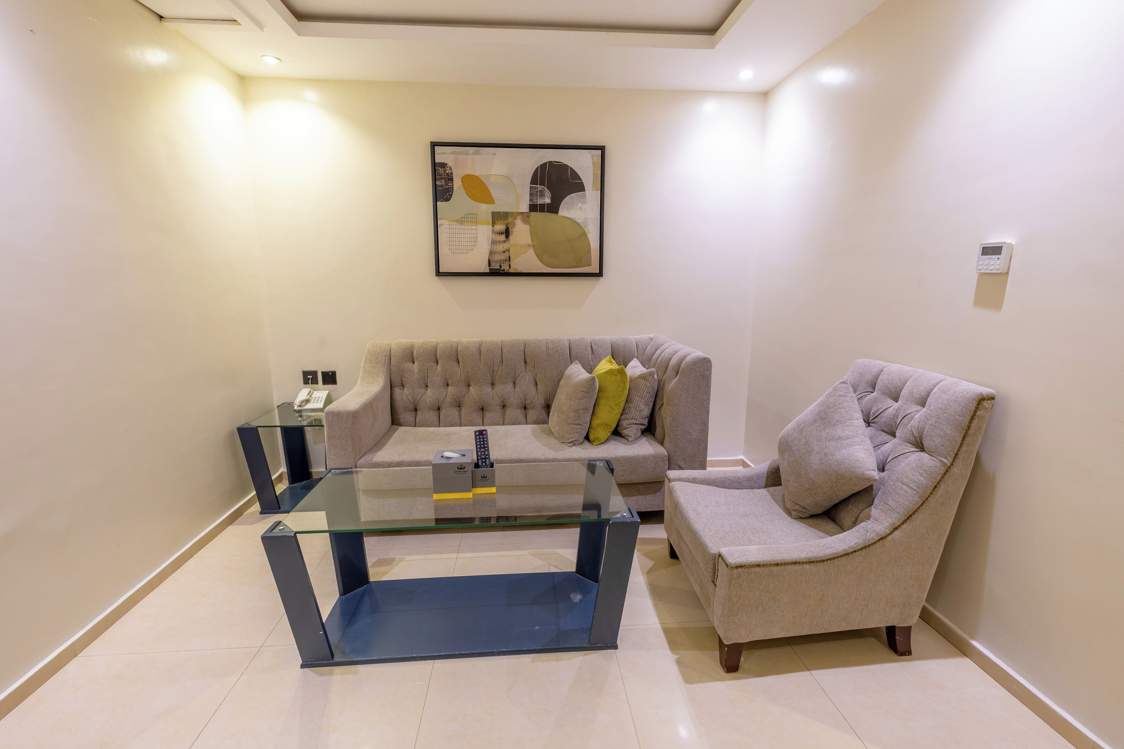 A modern living room with a glass coffee table, a tufted sofa, and a cushioned armchair.